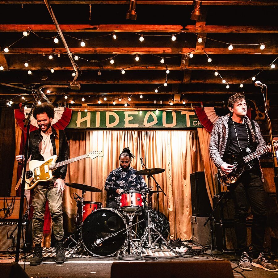 Hunter-gatherer on the Hideout stage in Chicago under strings of bulbs, the singer and bassist flanking a red drum kit beneath the green HIDEOUT sign